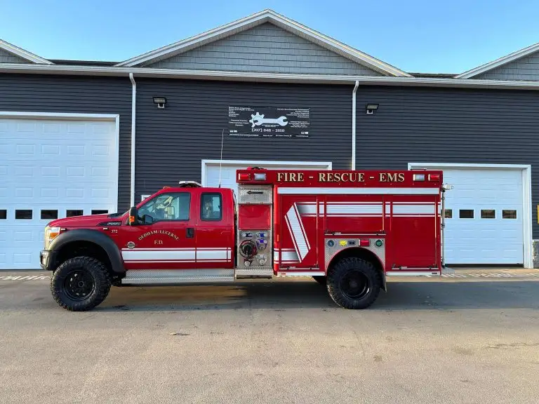 A bright red fire rescue truck with the words "FIRE - RESCUE - EMS" and "Spearville" on the side is parked in front of a grey building with two large white garage doors. The building also has a sign featuring a fire station logo above the doors.
